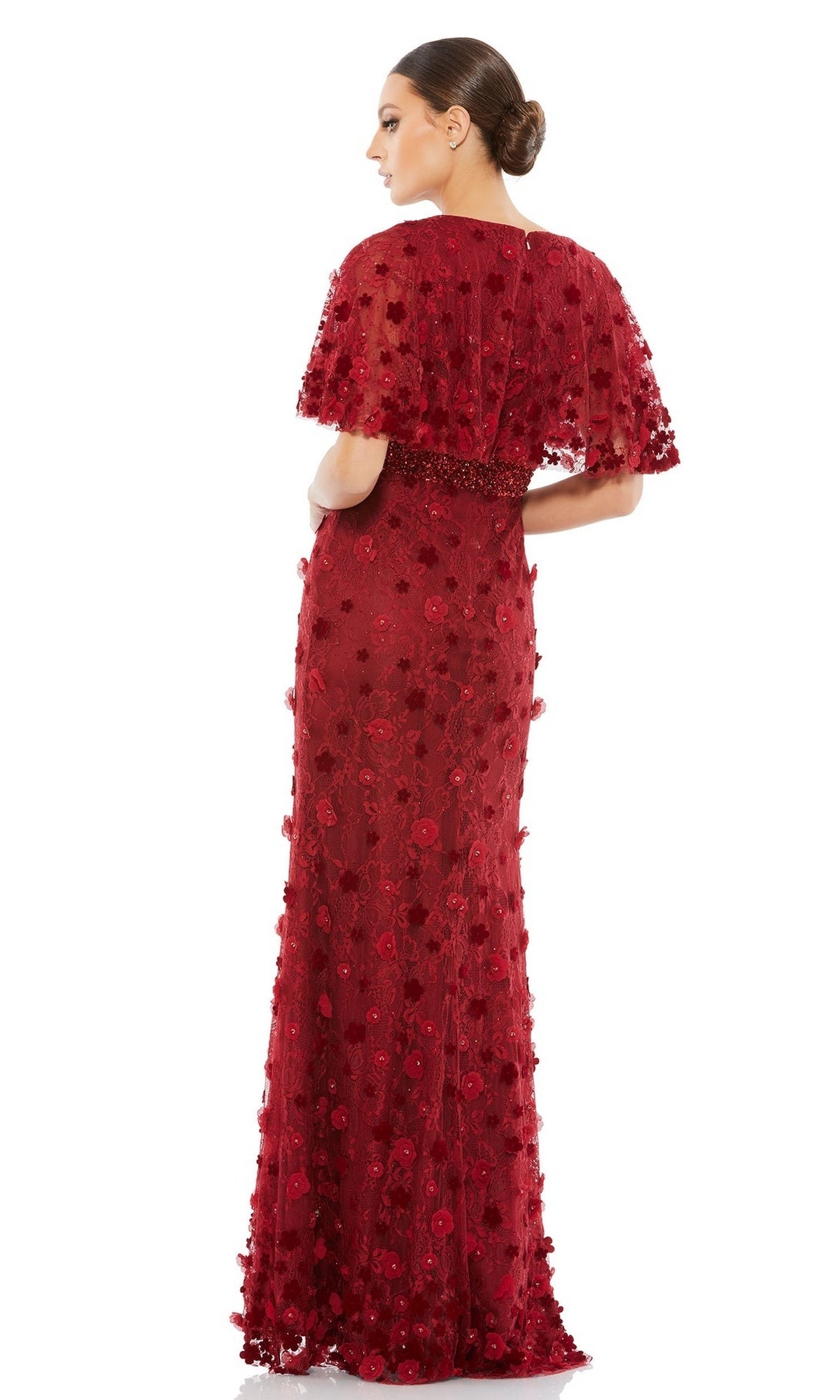 Woman poses with her back to the camera against a white background, wearing the Mac Duggal 67712 short-sleeve long formal dress, featuring textured red fabric, floral appliqués, and a cape overlay.